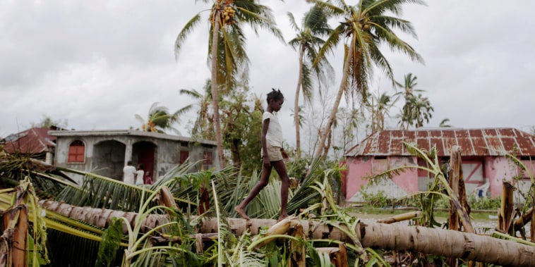Image: A girl walks on a tree damaged by Hurricane Matthew in Les Cayes
