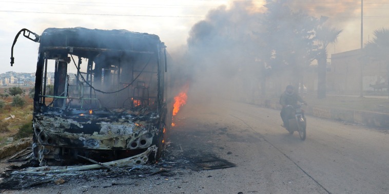 Image: A man on a motorcycle drives past burning buses