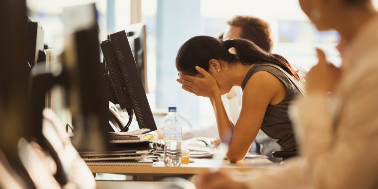 Image: Stressed woman sits with her head in her hands at an office desk