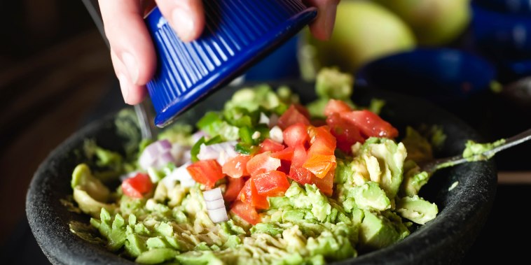 Image: A woman adds diced tomatoes and onions over a bowl of guacamole
