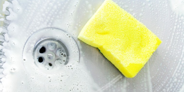 cleaning a kitchen sink with yellow sponge and cream cleanser