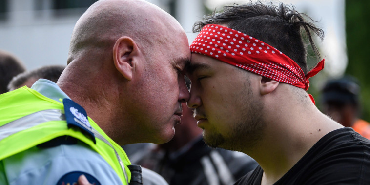 Image: A policeman and a biker gang member perform a hongi, a touching of noses, after a performance by different gang members of the haka as a tribute to victims in Christchurch