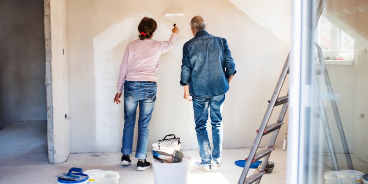 Rear View Of Senior Couple Painting Walls In New Home, Relocation Concept