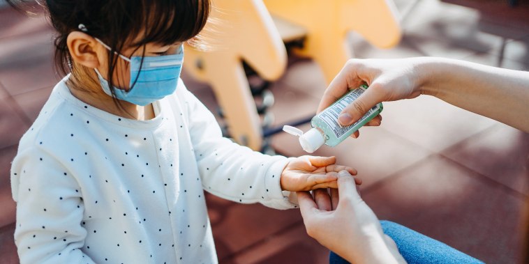 Young mother squeezing hand sanitizer onto little daughter's hand in the playground to prevent the spread of viruses