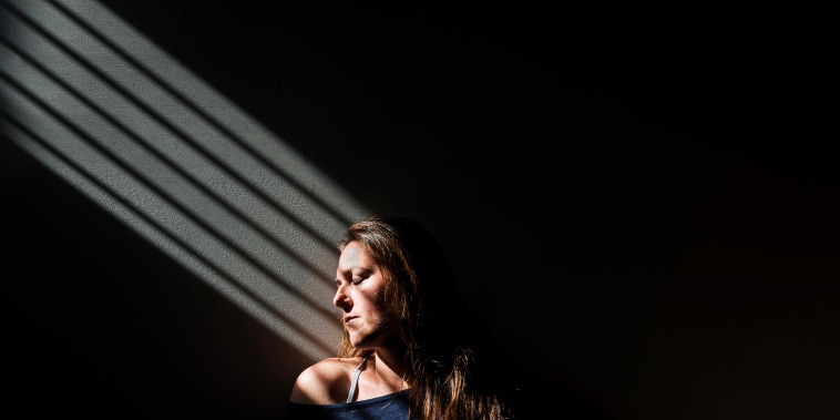Profile of a woman sitting in a patch of light in a darkened room.