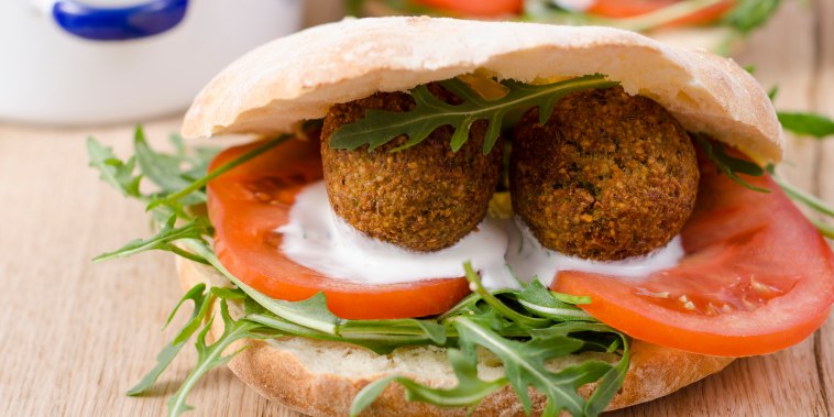 Homemade falafel, tomato, yoghurt sauce, rocket and mint in pita bread on chopping board