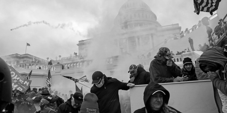 Supporters of President Donald Trump cover their faces to protect from tear gas during a clash with police in front of the Capitol on Jan. 6, 2021.
