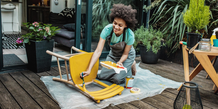 Woman paining a wooden chair yellow, outside on her patio