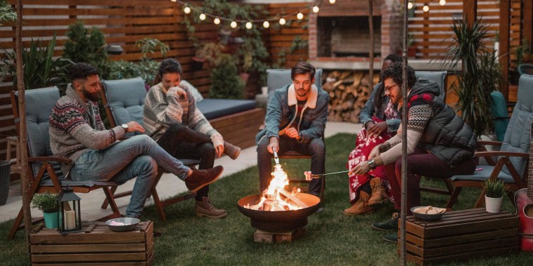 Group of friends in a backyard, roasting marshmallows over a fire pit