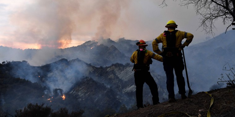 Firefighters work on a fire line as flames from the Palisades Fire glow in the distance in Topanga State Park, northwest of Los Angeles, on May 15, 2021.