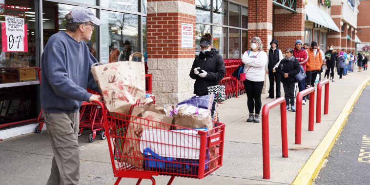 A shopper passes near a self-distancing queue outside Trader Joe's in Bailey's Crossroads, Va., on March 31, 2020.