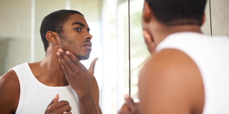 Man applying moisturizer to his face, while looking in the mirror