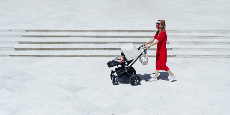 Mother wearing mask pushing son in baby carriage while walking on town square