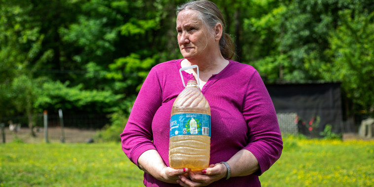 Hazel Cooper holds a jug of orange, contaminated water from one of her two wells. She and her husband have about $50 left every month after paying their bills, and use the money to buy bottled water.