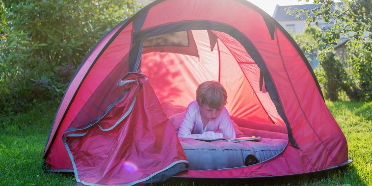Boy reading in a red tent at evening twilight on an air mattress