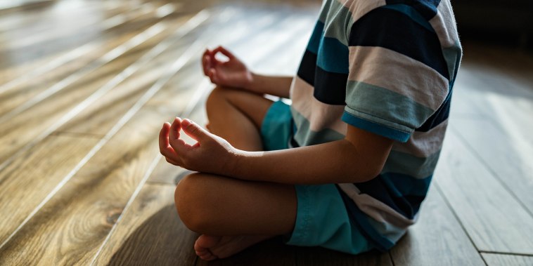 Unrecognizable little kid meditating in Lotus position at home.