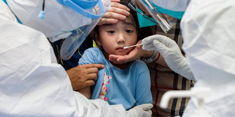 Image: A child is held as medical staff swab for Covid in Wuhan, China
