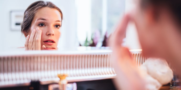Woman applying makeup in front of a big mirror.
