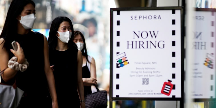 A sign advertising job openings is seen while people walk into the store in New York on Aug. 6, 2021.