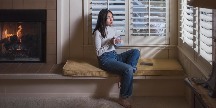 Young woman inside home wearing sweater drinking from a mug