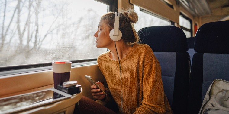 Photo of a young woman riding on a train, enjoying her trip while looking through the window and listening to some music on her mobile phone
