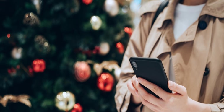 shot of a woman using smartphone in front of a colourful Christmas tree in the festive Christmas season