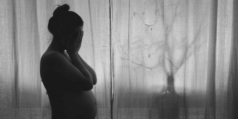 A pregnant woman holds her face in her hands.