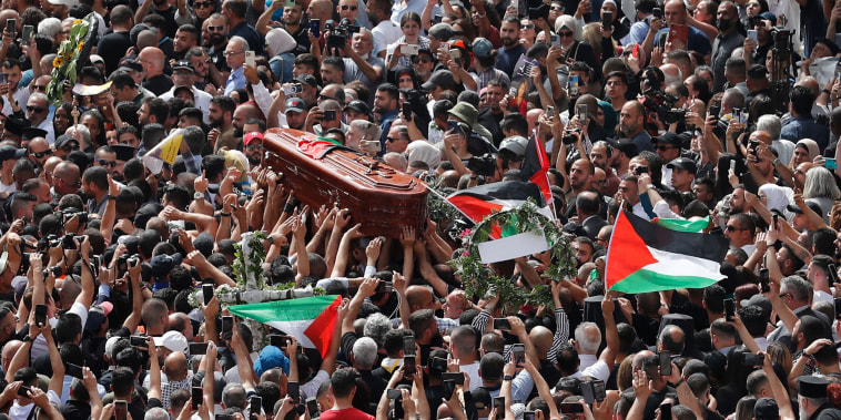 Image: Mourners wave national flags as they carry the casket during a funeral procession.