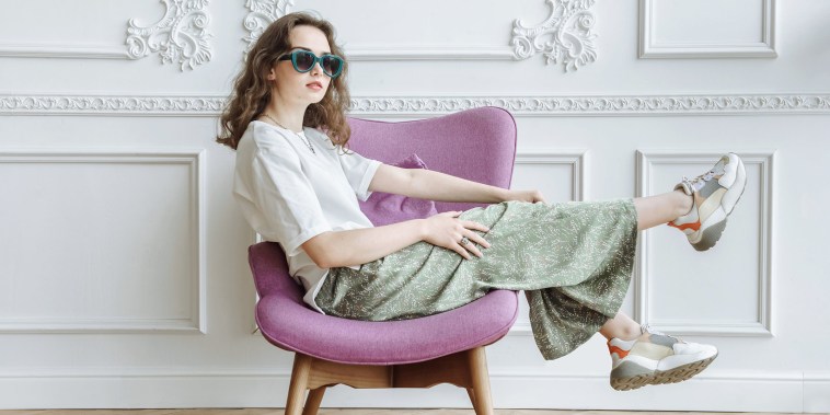 Brunette woman model in sunglasses posing in studio sitting on armchair