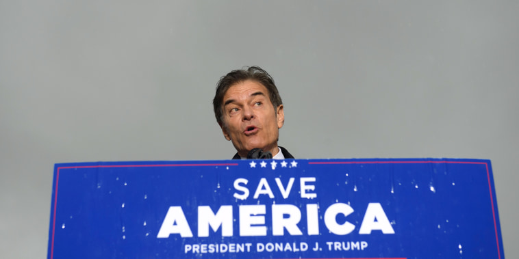 Image: Dr. Mehmet Oz standing behind a podium with a sign that reads,\"Save America, President Donald j. Trump\".