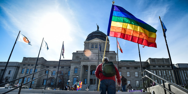 A man holds a Pride flag on the steps of the Montana State Capitol