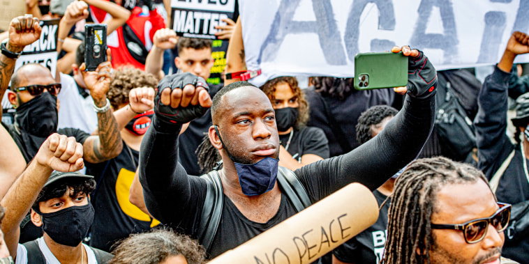 A Black man raising his fist up records a video with his phone of the \"Black Lives Matter\" protest in Amsterdam on June 1, 2020.