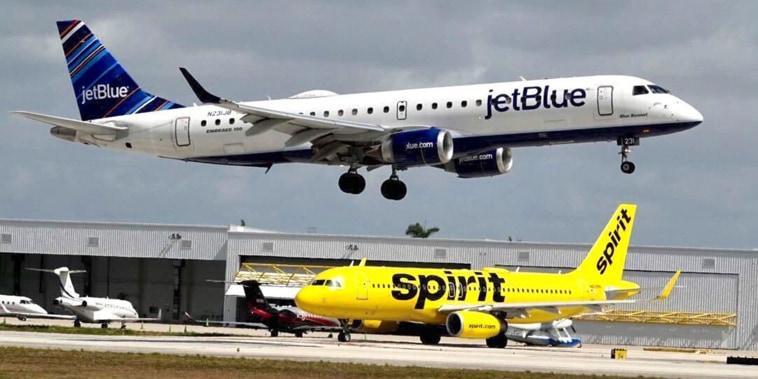 A JetBlue airliner lands past a Spirit Airlines jet