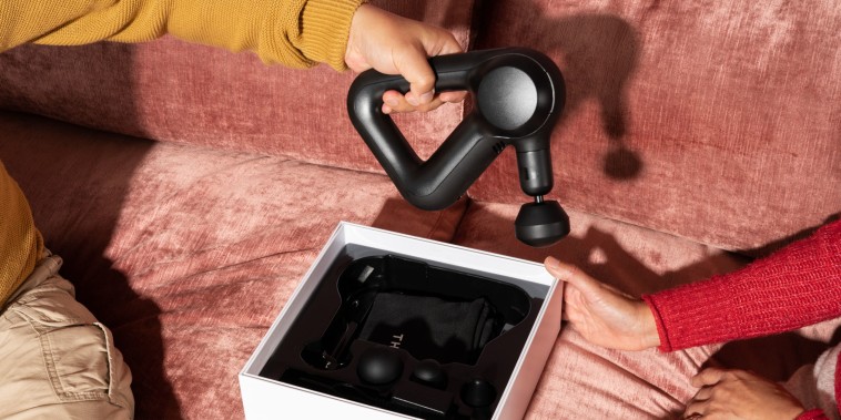 Hand holding a massage gun over a couch