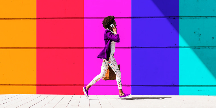 Young woman talking on smart phone while walking by colorful wall during sunny day