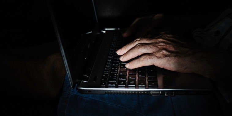 Anonymous aged person using laptop in darkness