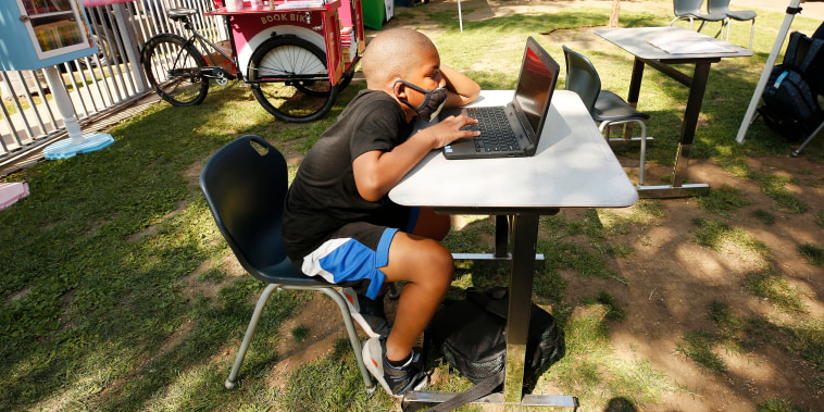 A student works on a laptop computer with other kids studying outdoors in the motel plaza area at Hyland Motel in Van Nuys, Calif., on Aug. 24, 2020.