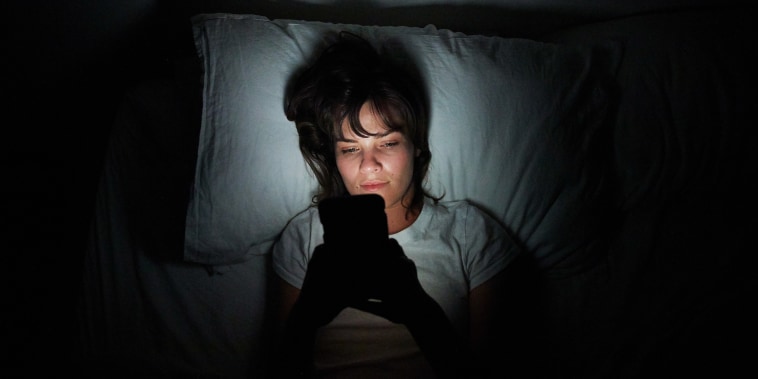 Young woman lying in bed at night using her cellphone