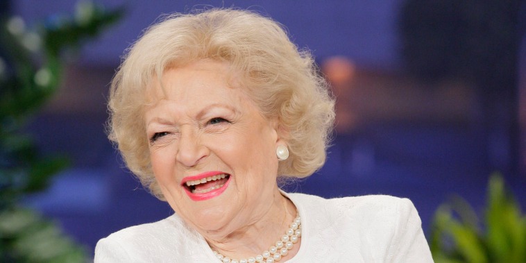 Betty White in a white top and pearls smiles and laughs.