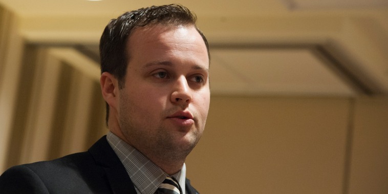 A close up photo of Josh Duggar  in a suit and tie in a generic beige conference room.