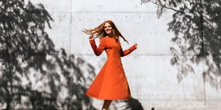 A single woman dances in an orange dress while outside.