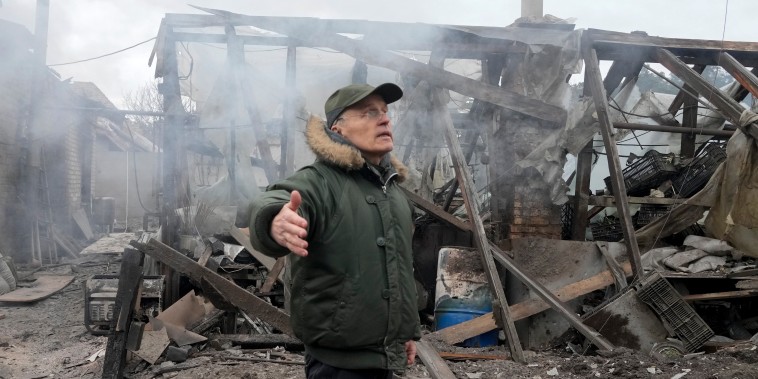A man opens his arms as he stands near a house destroyed in the Russian artillery shelling, in the village of Horenka close to Kyiv, Ukraine, Sunday, March 6, 2022.