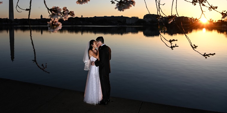 As the sun rises, a couple from Arlington, Va., kiss as they have a photo shoot in their wedding attire along the Tidal Basin as people gather for the blooming cherry blossoms on March 21, 2022 in Washington, DC.