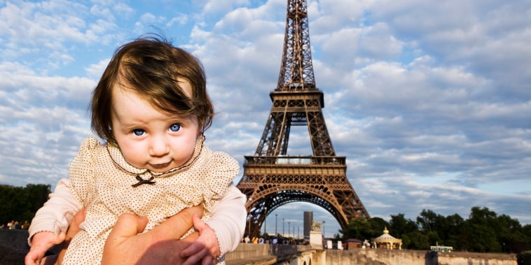 A baby being held aloft in front of the Eiffel Tower, Paris, France