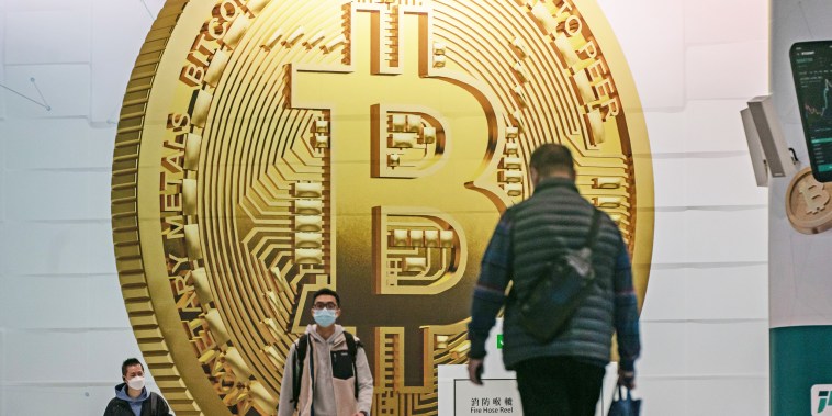 Pedestrians walk past an advertisement displaying a Bitcoin