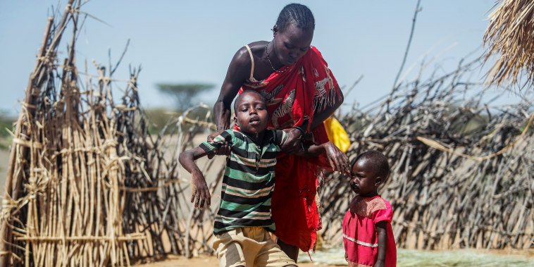 A mother helps her malnourished son stand after he collapsed near their hut in the village of Lomoputh in northern Kenya, on May 12, 2022.