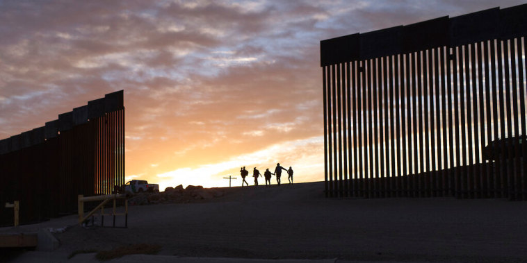 Un par de familias migrantes de Brasil pasan a través de una brecha en el muro fronterizo para llegar a Estados Unidos después de cruzar de México a Yuma, Arizona, para buscar asilo, en junio de 2021.
