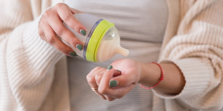 Unrecognizable mom tests the temperature of a baby bottle
