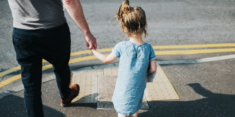 Little girl holding her Father's hand, about to cross a Road