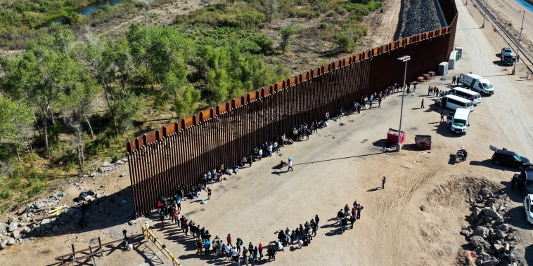 Immigrants wait in line to be processed by the U.S. Border Patrol after crossing through a gap in the U.S.-Mexico border barrier in Yuma, Ariz. on May 21, 2022.